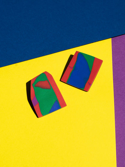 Front view of two original Salvaje studs, handmade in polymer clay, photographed on a colourful background under direct sunlight.