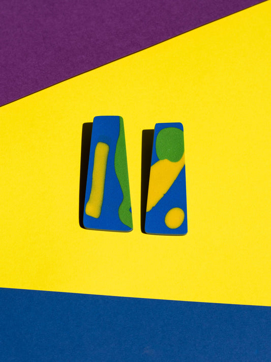 Front view of two original Salvaje studs, handmade in polymer clay, photographed on a colourful background under direct sunlight.