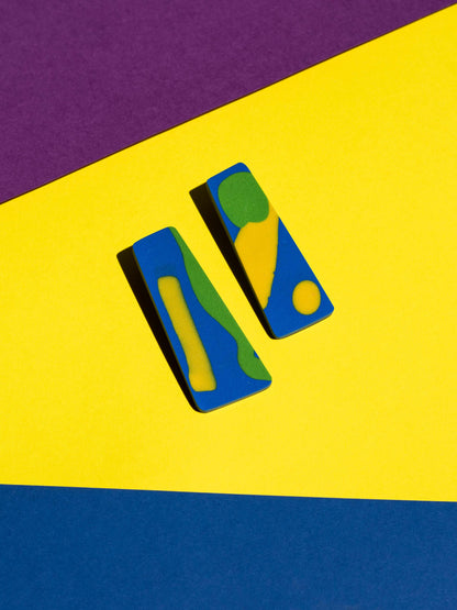 Front view of two original Salvaje studs, handmade in polymer clay, photographed on a colourful background under direct sunlight.