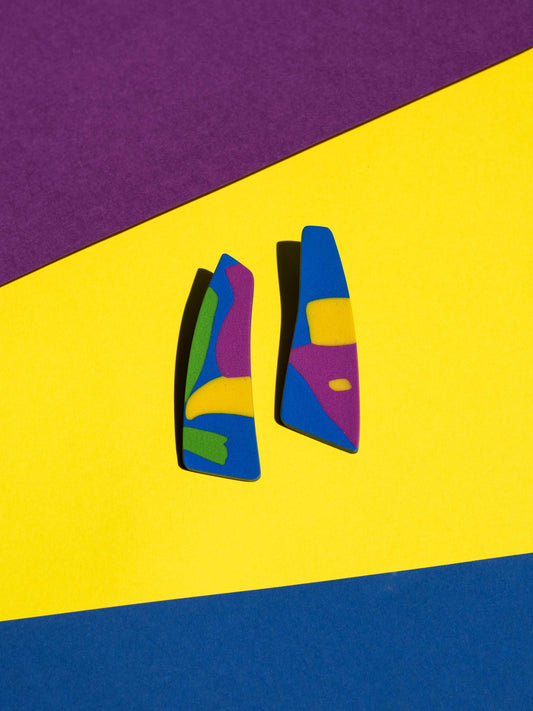 Front view of two original Salvaje studs, handmade in polymer clay, photographed on a colourful background under direct sunlight.