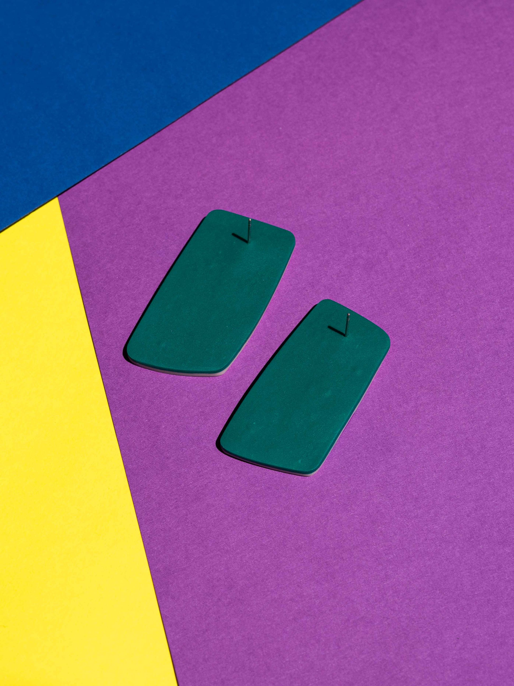 Back view of two original Salvaje studs, handmade in polymer clay, photographed on a colourful background under direct sunlight.