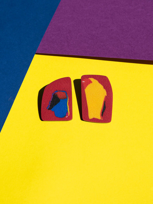 Front view of two original Salvaje studs, handmade in polymer clay, photographed on a colourful background under direct sunlight.