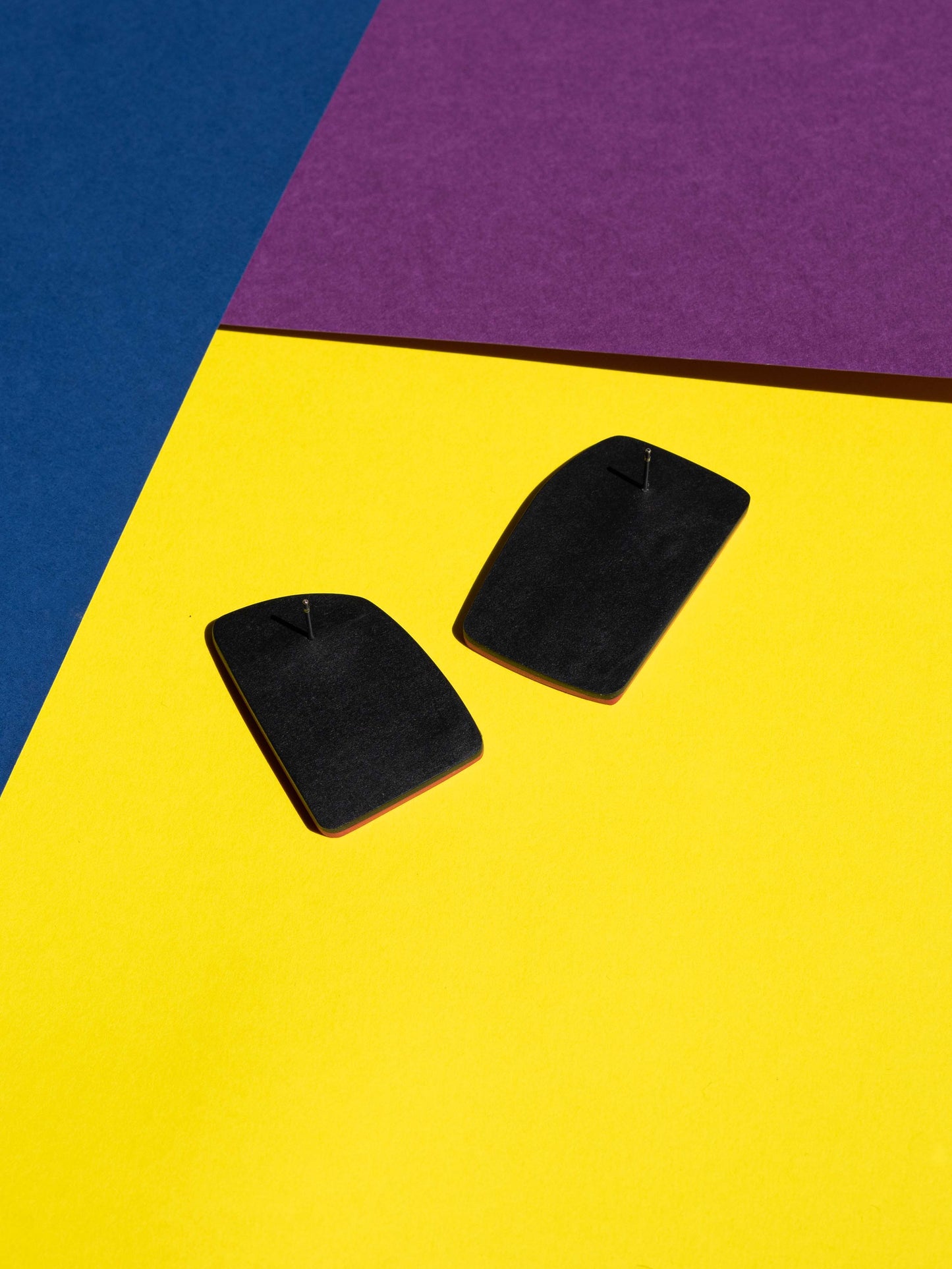 Back view of two original Salvaje studs, handmade in polymer clay, photographed on a colourful background under direct sunlight.
