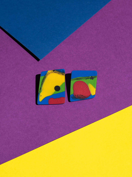 Front view of two original Salvaje studs, handmade in polymer clay, photographed on a colourful background under direct sunlight.