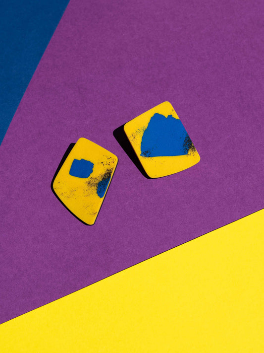 Front view of two original Salvaje studs, handmade in polymer clay, photographed on a colourful background under direct sunlight.