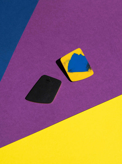 Front and back views of two original Salvaje studs, handmade in polymer clay, photographed on a colourful background under direct sunlight.