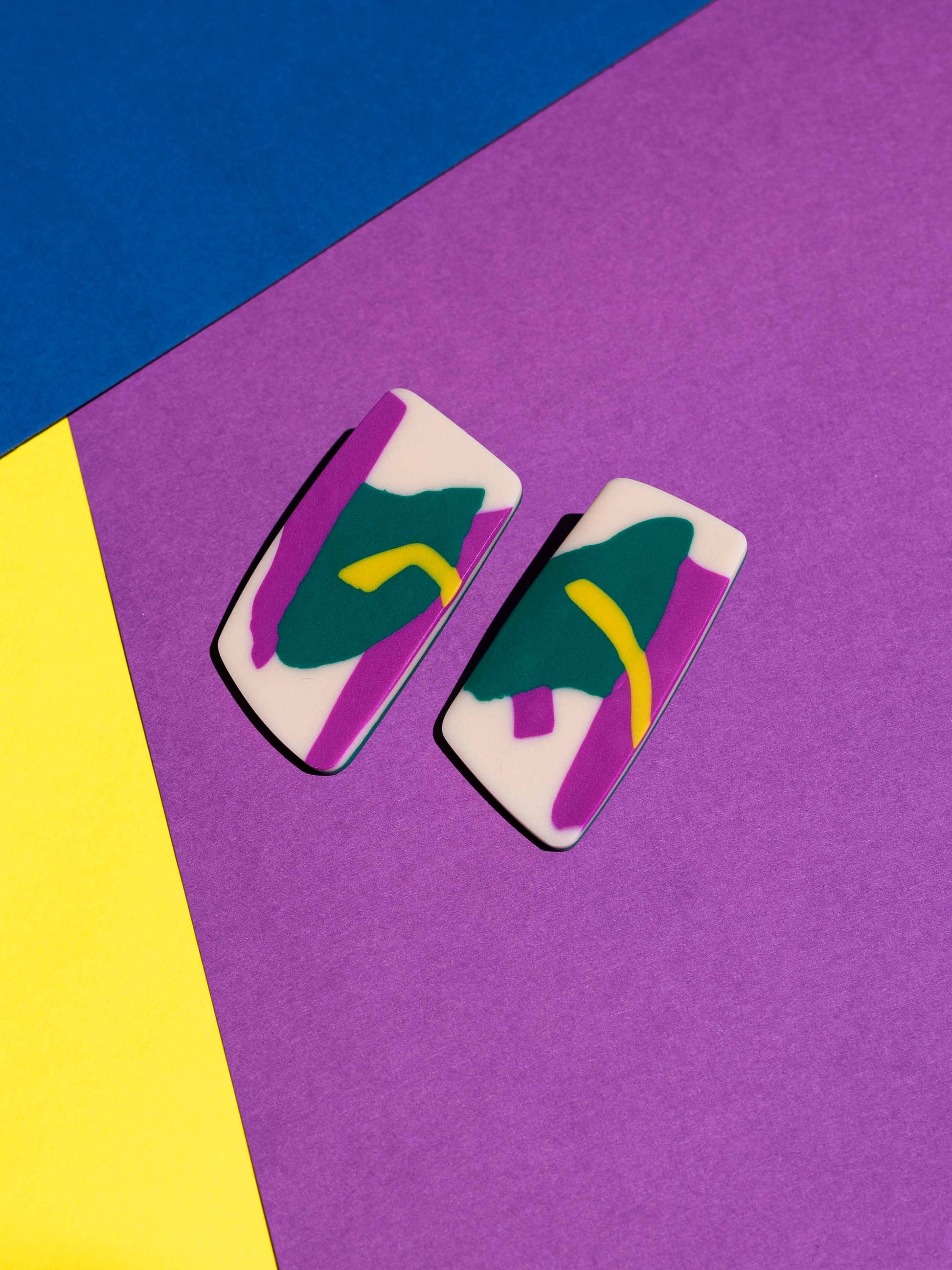 Front view of two original Salvaje studs, handmade in polymer clay, photographed on a colourful background under direct sunlight.