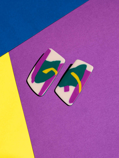 Front view of two original Salvaje studs, handmade in polymer clay, photographed on a colourful background under direct sunlight.