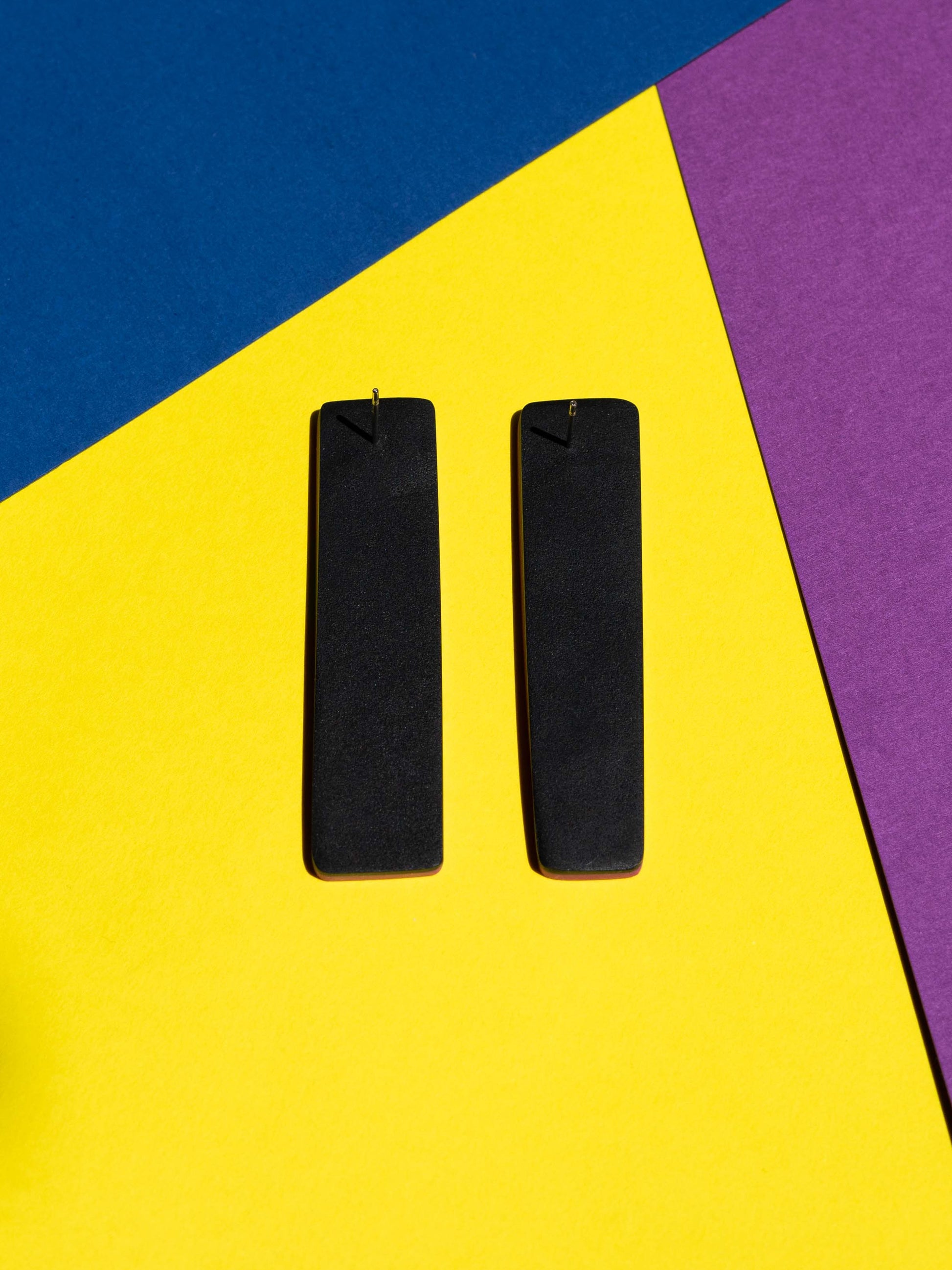 Back view of two original Salvaje studs, handmade in polymer clay, photographed on a colourful background under direct sunlight.